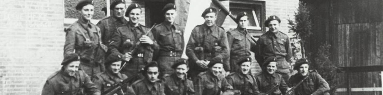 Militaire eenheid poseert voor gebouw op zwart-witfoto uit Tweede Wereldoorlog.