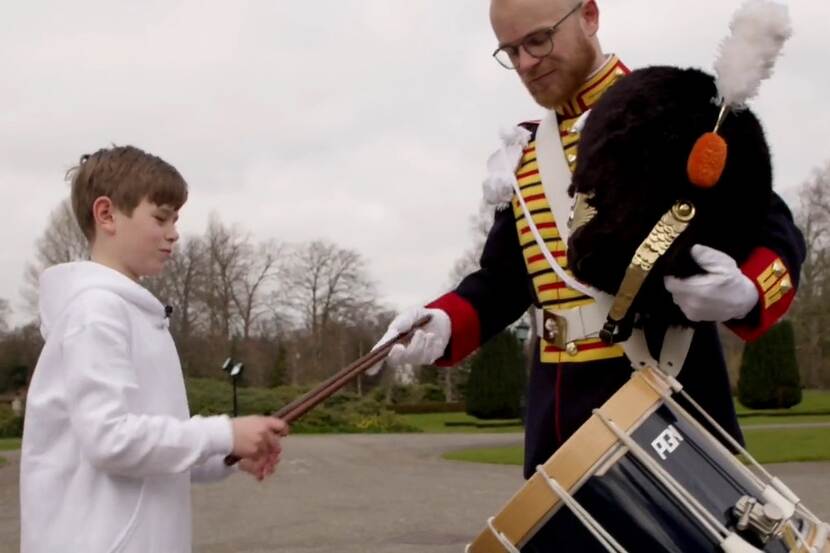Een jongen van Koorschool Haarlem krijgt tijdens de opnames van de clip de trommelstokken van een militair van de Regimentsfanfare ‘Garde Grenadiers en Jagers'.