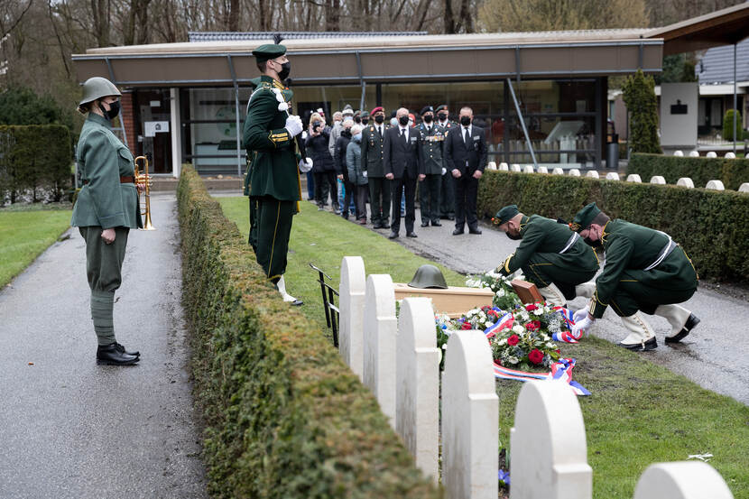 Militairen leggen bloemen bij het graf. Er achter staat een trompettist in een Nederlands uniform uit de Tweede Wereldoorlog.