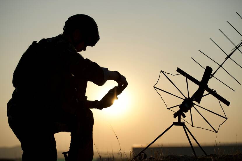 Een militair en een antenne van communicatieapparatuur steken af tegen een verlichte lucht.