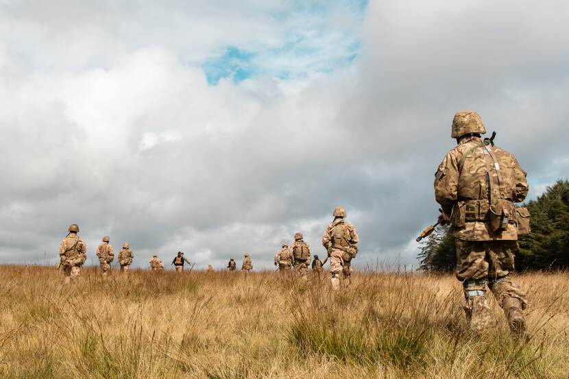 Militairen lopen door graslandschap.