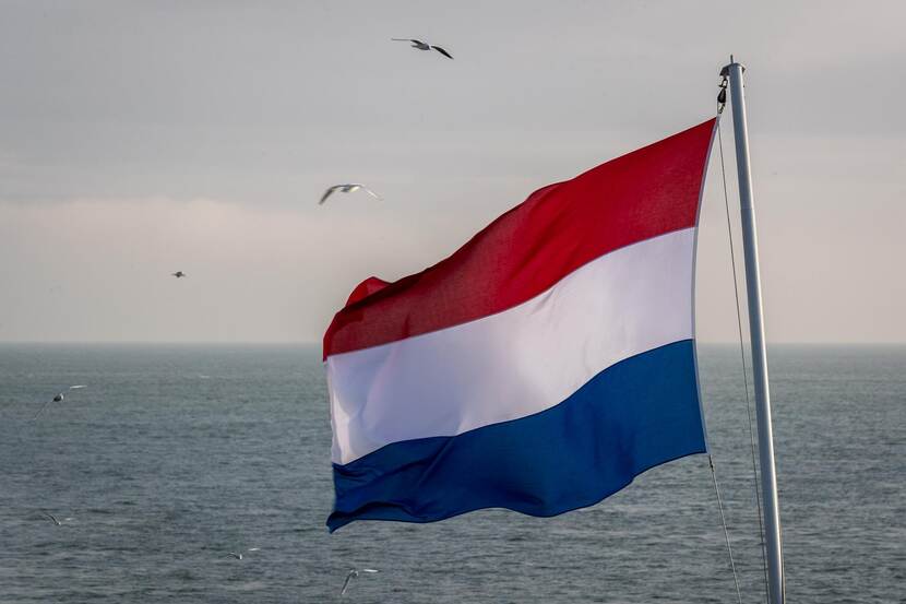 Wapperende Nederlandse vlag met een zee als achtergrond.