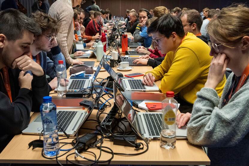 Een groep mensen werkt aan een lange tafel op laptops.