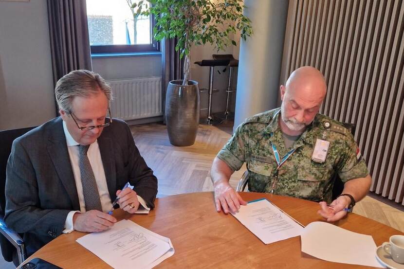Een man in pak en een man in militair uniform tekenen een contract aan tafel.