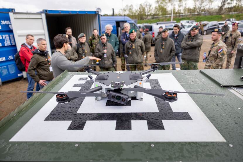Militairen kijken naar een platform waarop een drone staat. Iemand geeft uitleg.