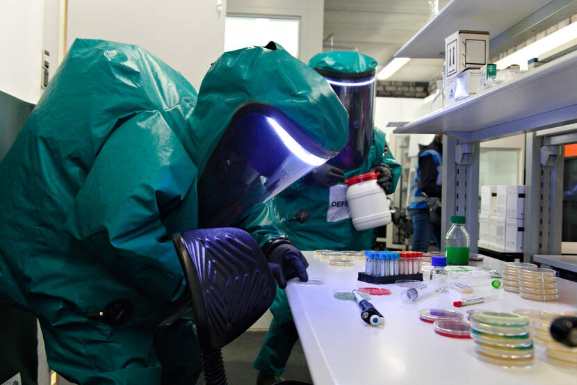 Personen in beschermende pakken onderzoeken petrischaaltjes in een lab.