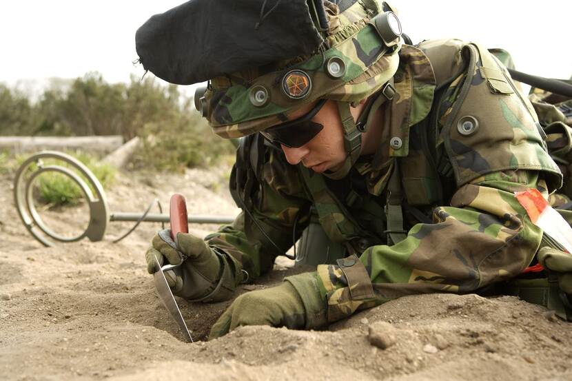 Een militair in opleiding graaft een gat in het zand.