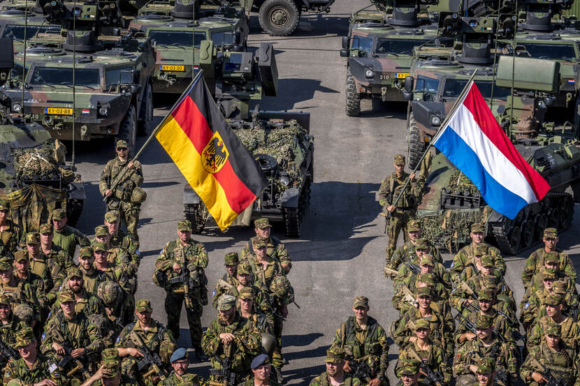 Nederlandse en Duitse militairen defileren met de Nederlandse en Duitse vlag.