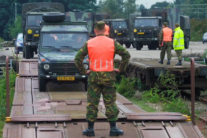 Militair begeleidt voertuigen op een wagon.
