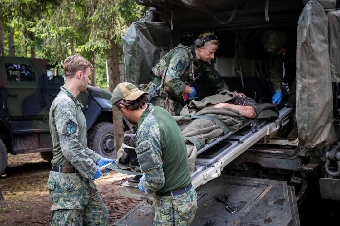 3 militairen dragen een vierde op een brancard een voertuig in