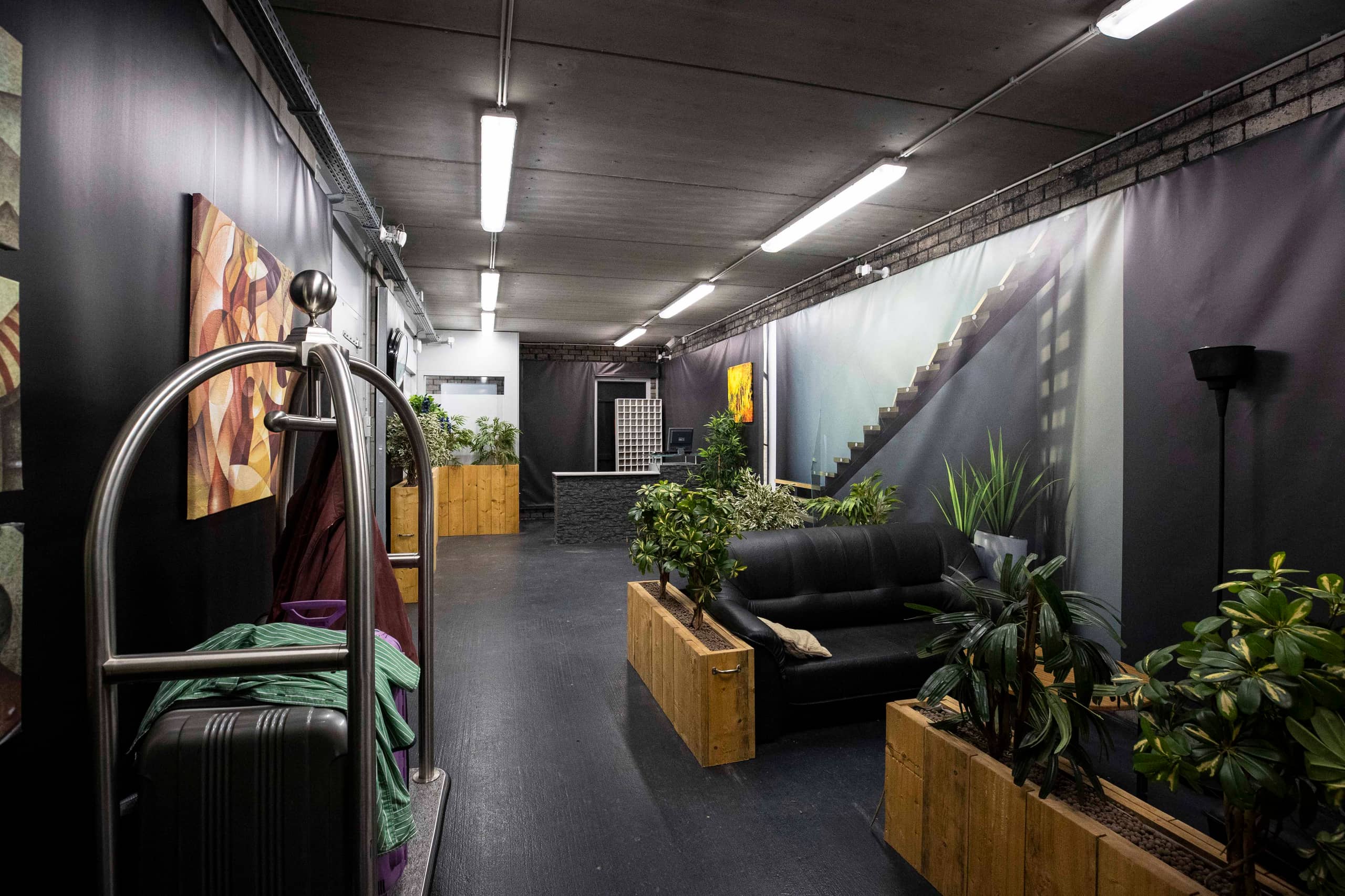 Hotellobby met plantenbakken, koffers en zitgedeelte.