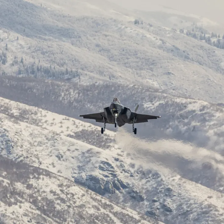 Een F-35 vliegend boven besneeuwd berglandschap.
