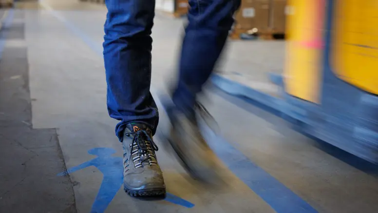 Een persoon met wandelschoenen beweegt zich langs een blauwe lijn. Daarnaast is een blauw poppetje afgebeeld, om aan te geven waar je mag lopen. 