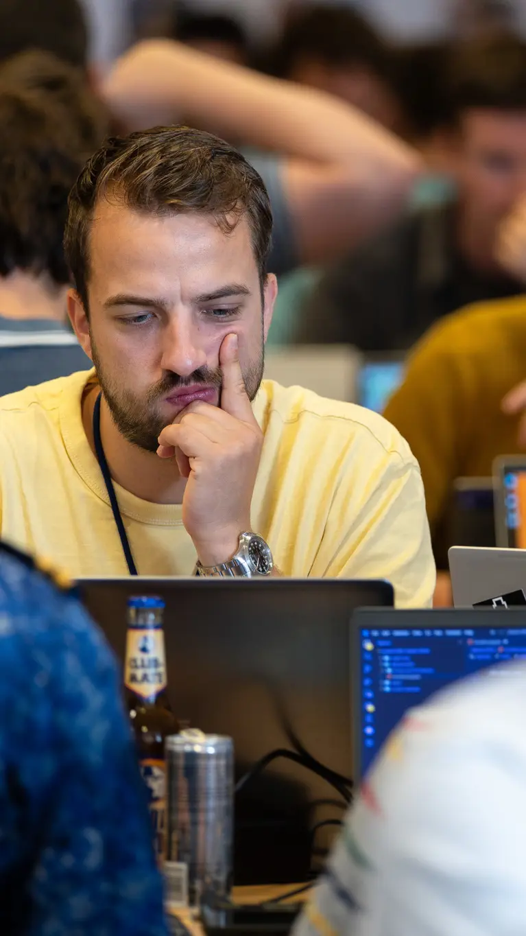 Man in geel t-shirt kijkt fronsend naar zijn laptopscherm met tegenover hem iemand van de marine.