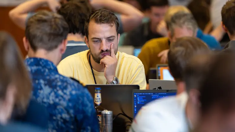 Man in geel t-shirt kijkt fronsend naar zijn laptopscherm met tegenover hem iemand van de marine.