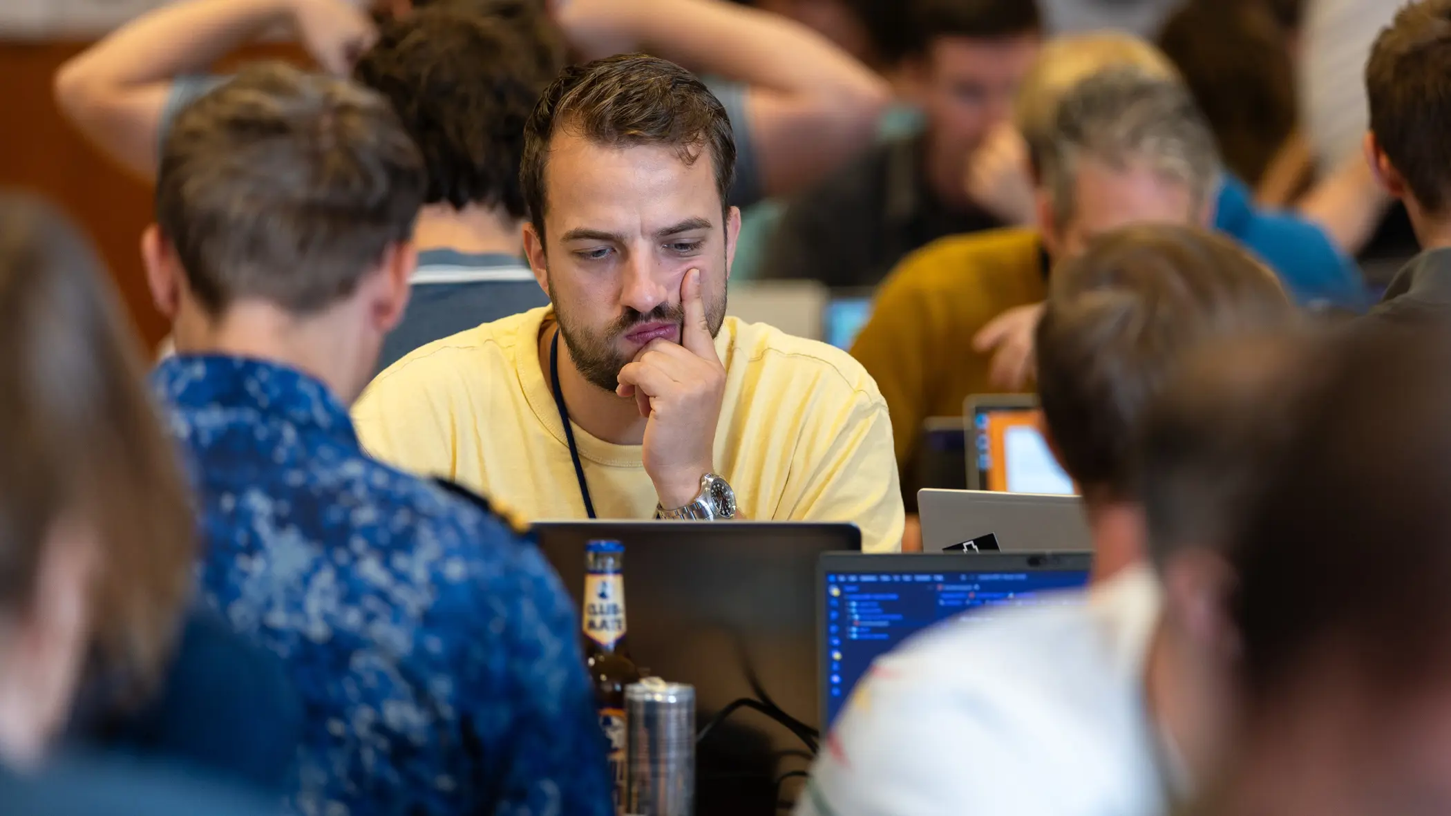 Man in geel t-shirt kijkt fronsend naar zijn laptopscherm met tegenover hem iemand van de marine.