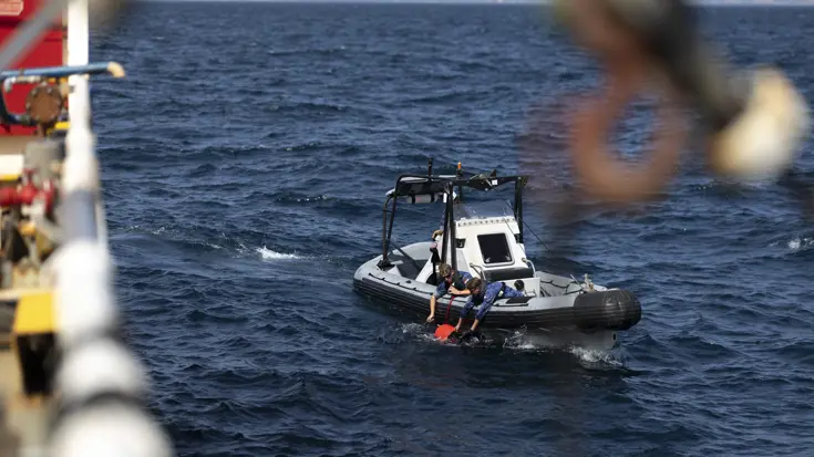 Militairen van de marine hangen over de rand van een RHIB-motorboot en halen een roodkleurig systeem uit het water.