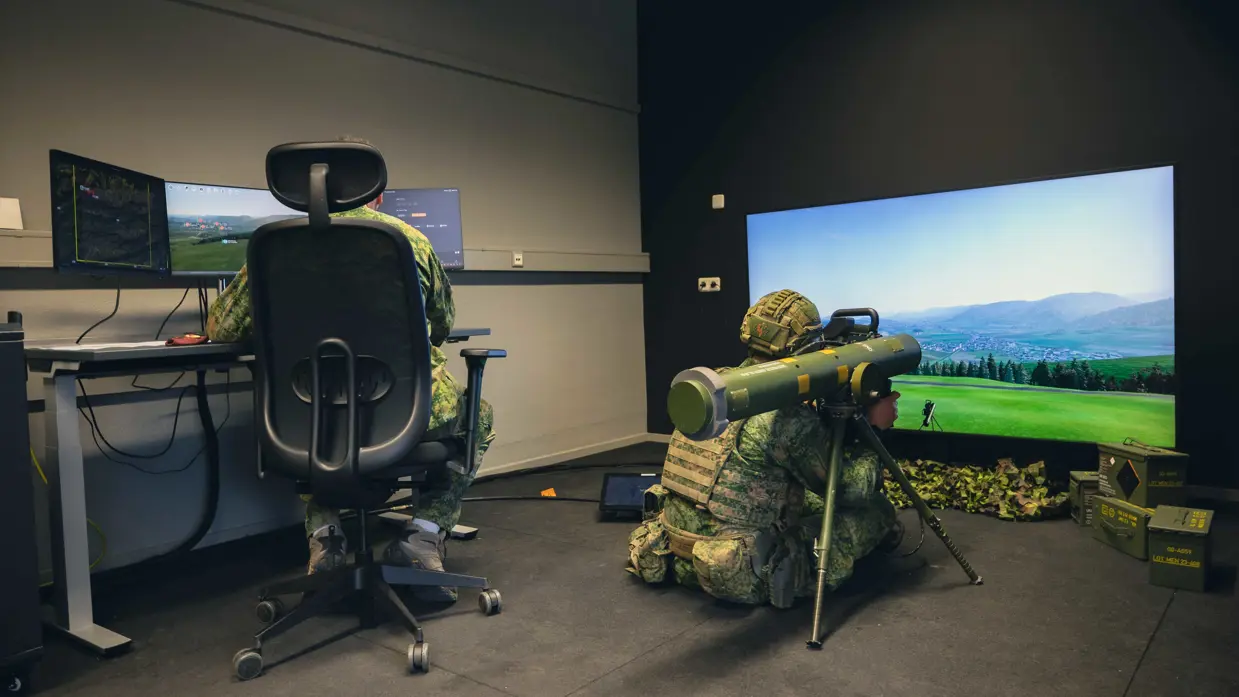 Een viertal afbeeldingen. Naast het cilindervormige, donkergroene antitankwapen Spike Long Range gericht op een beamer, hetzelfde middel alleen nu met daarachter een militair. Samen met een instructeur, die achter een beeldscherm zit, bevinden de twee zich in een kleinere ruimte. Vervolgens diezelfde oefenende militair schuin vanaf onder en gezien vanaf voren. Daarbij is zijn geconcentreerde blik zichtbaar.