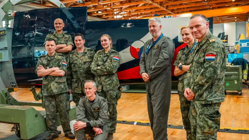 Acht militairen van verschillende eenheden poseren in een hal voor het nieuwe toestel. 