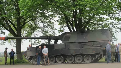 Deelnemers aan de excursie staan rondom een militair voertuig en aanschouwen dat.
