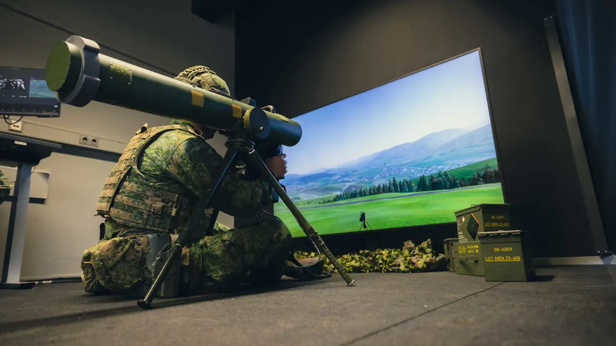 Een viertal afbeeldingen. Naast het cilindervormige, donkergroene antitankwapen Spike Long Range gericht op een beamer, hetzelfde middel alleen nu met daarachter een militair. Samen met een instructeur, die achter een beeldscherm zit, bevinden de twee zich in een kleinere ruimte. Vervolgens diezelfde oefenende militair schuin vanaf onder en gezien vanaf voren. Daarbij is zijn geconcentreerde blik zichtbaar.