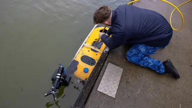 Een marinecollega zit gebogen op de kade en is bezig met een geel vaartuigje dat half onder water ligt. Op de andere foto bedient een marinecollega joysticks en kijkt naar een beeldscherm waarop onderwaterbeelden te zien zijn. 