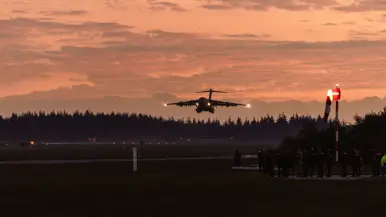 Een groot vrachtvliegtuig landt in de rode ochtendschemer.