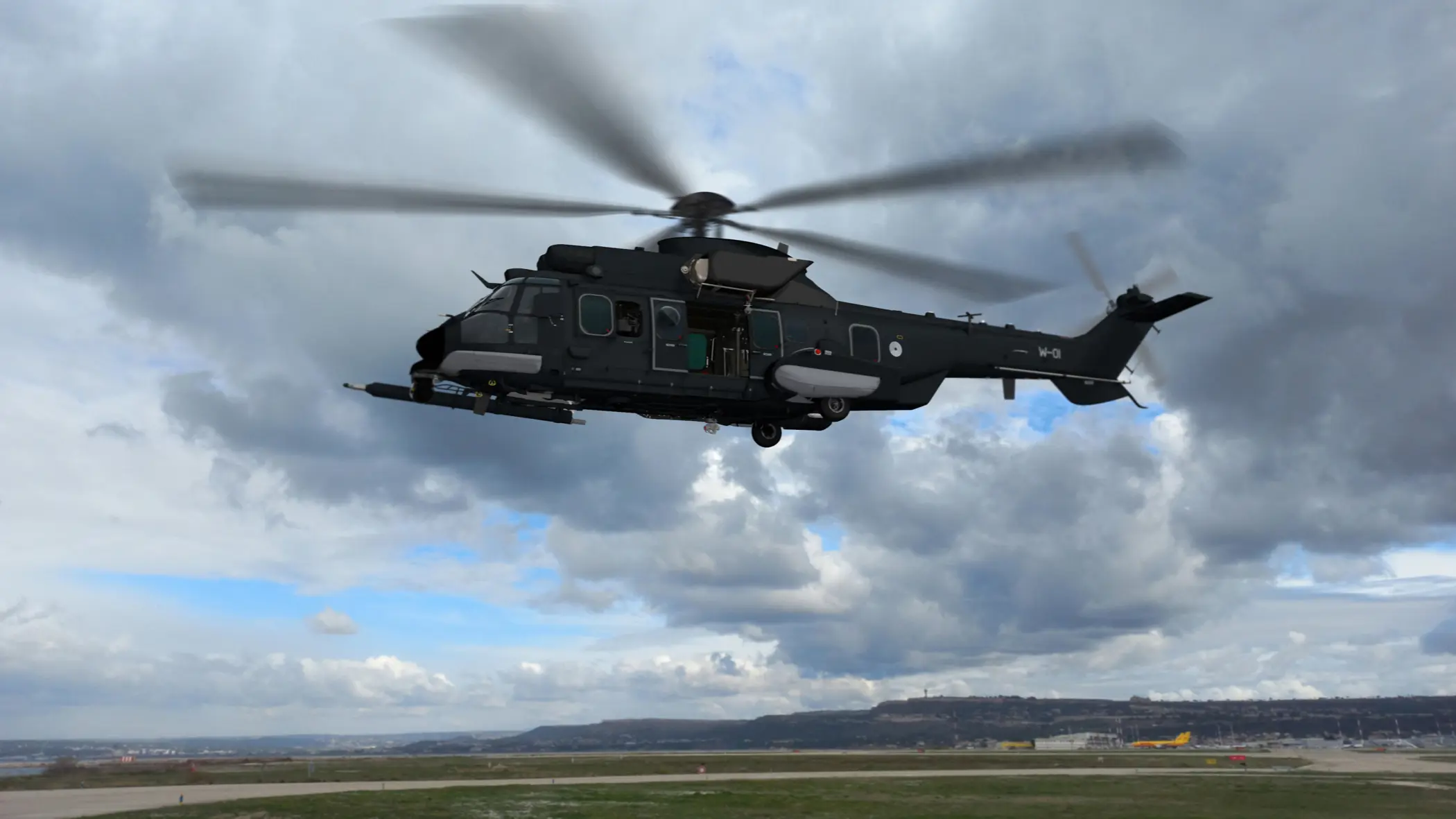 Een donkergrijze helikopter vliegt boven een vliegveld.