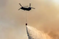 Chinook-transporthelikopter in oranjegekleurde lucht stort water uit met bambi-bucket onder het toestel.