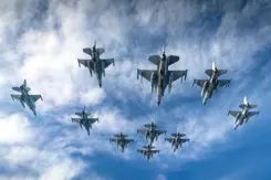 Een formatie F-16 vliegtuigen van onderaf gezien. Een blauwe lucht op de achtergrond met enkele wolken.