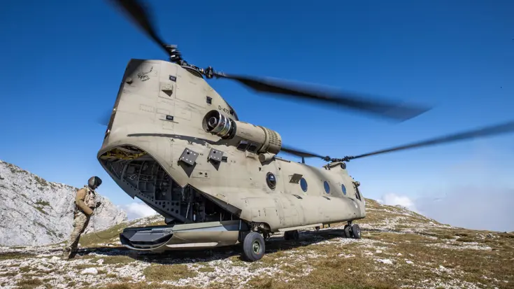Loadmaster achter Chinook-transporthelikopter, die in de bergen staat.