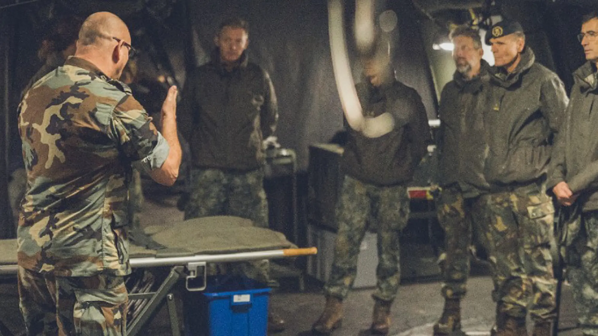 Instructeur staat naast een bed en apparatuur in een tent van het veldhospitaal terwijl hij groep militairen uitleg geeft.