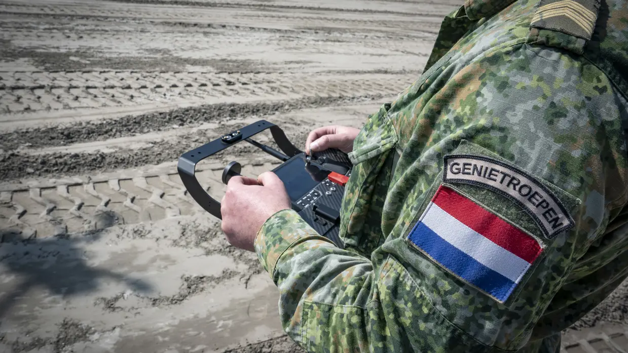 Een militair bedient een console voor een drone. Van de militair is enkel de romp te zien. Op zijn arm prijkt een eenheidsembleem van de genietroepen, plus een Nederlandse vlag.