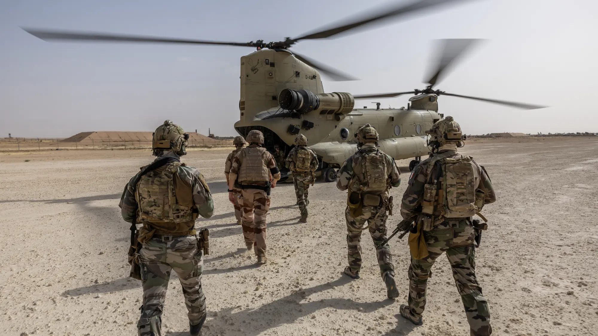 Militairen lopen richting Chinook in woestijnachtige omgeving.