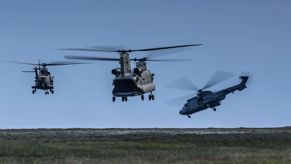 Drie helikopters vliegen laag boven de grond.