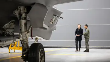 Staatssecretaris Tuinman in groen pak staat de pers te woord. Minister Brekelmans praat onder een luchtmachter bij een F-35.
