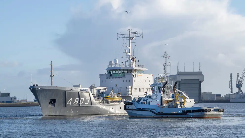 Een varende Zr.Ms. Luymes met een sleepboot erbij.
