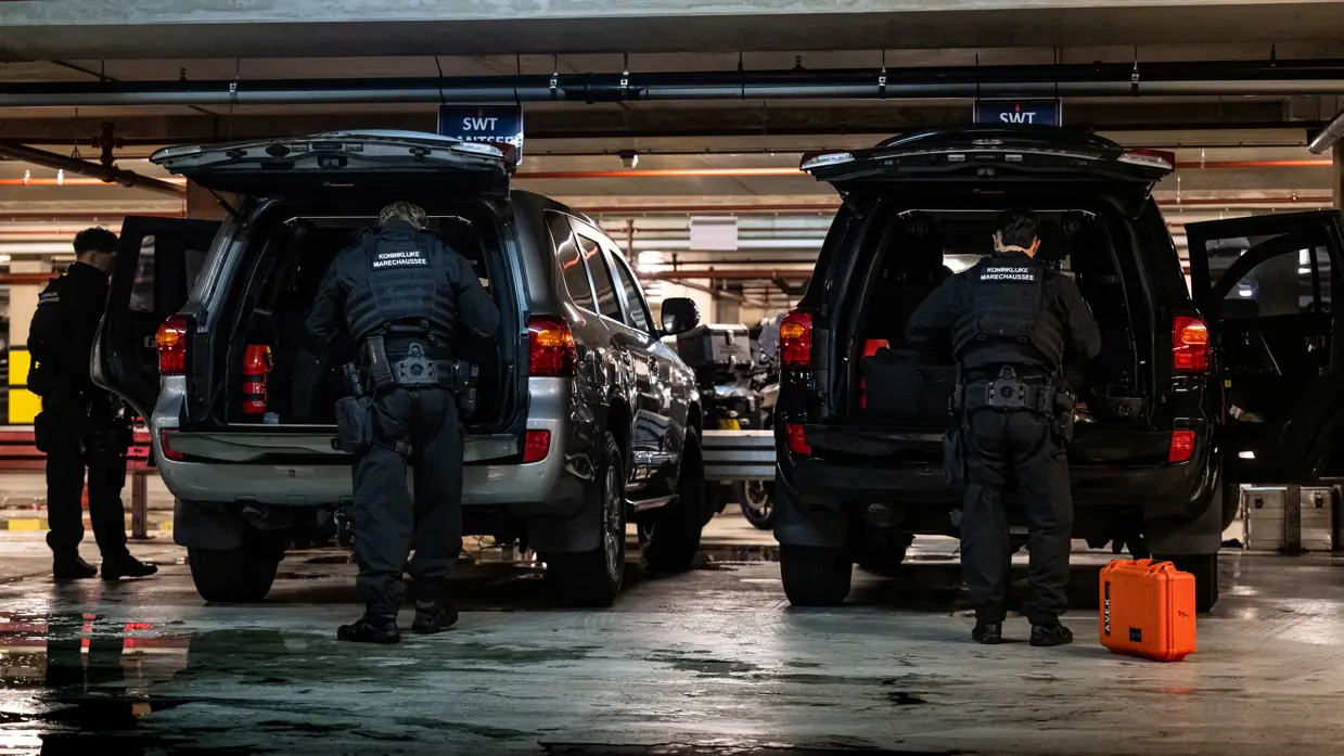 Marechaussees laden en controleren materieel in dienstvoertuigen in een parkeergarage.
