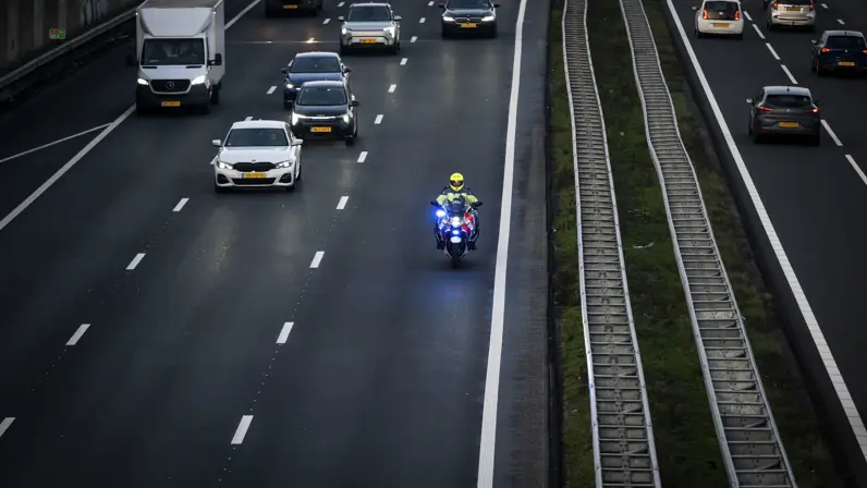 Een motorbegeleider van de Koninklijke Marechaussee rijdt met zwaailicht over de snelweg terwijl het overige verkeer ruimte maakt.