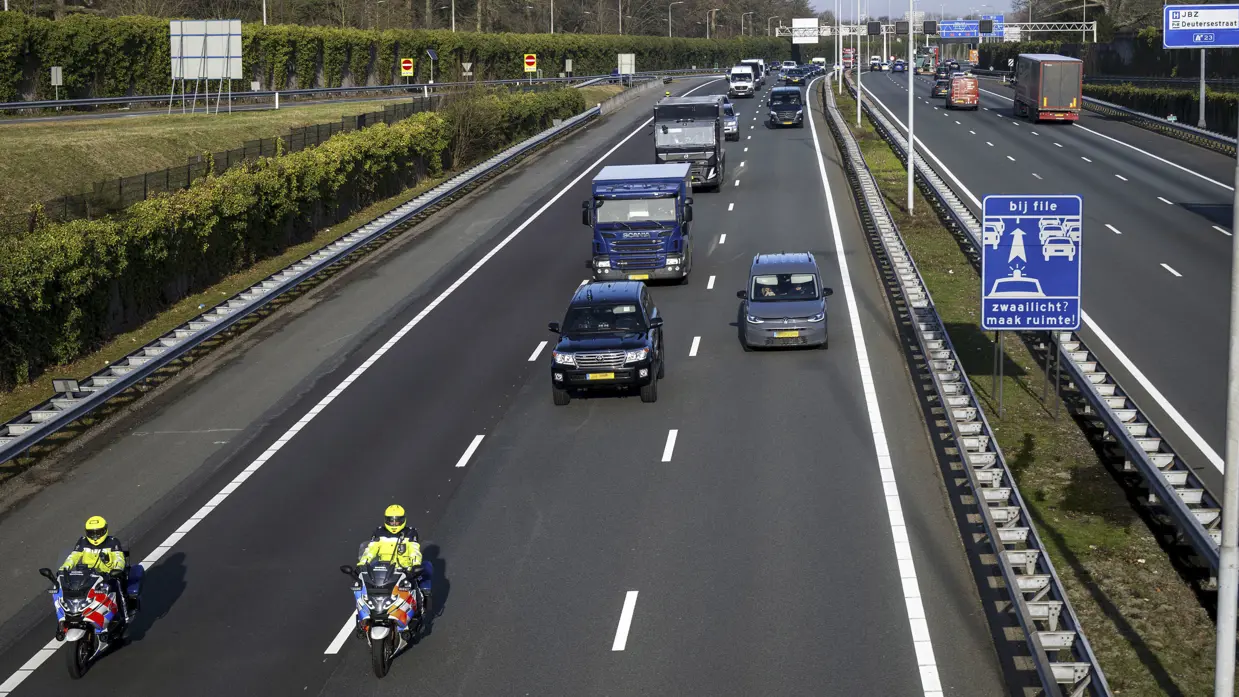 Motorbegeleiders van de Koninklijke Marechaussee rijden voor een colonne dienstvoertuigen over de snelweg.