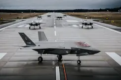 7 F-35's staan op een landingsbaan. De voorste is zichtbaar vanaf de zijkant. Van de overige 6 is de neus te zien.