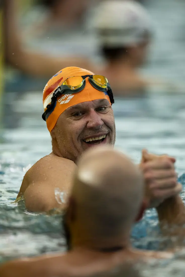 2 zwemmers in het water geven elkaar een hand.