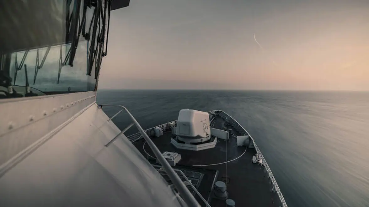 Beeld vanaf de brug van een varend fregat, het boordkanon duidelijk zichtbaar op het voordek.