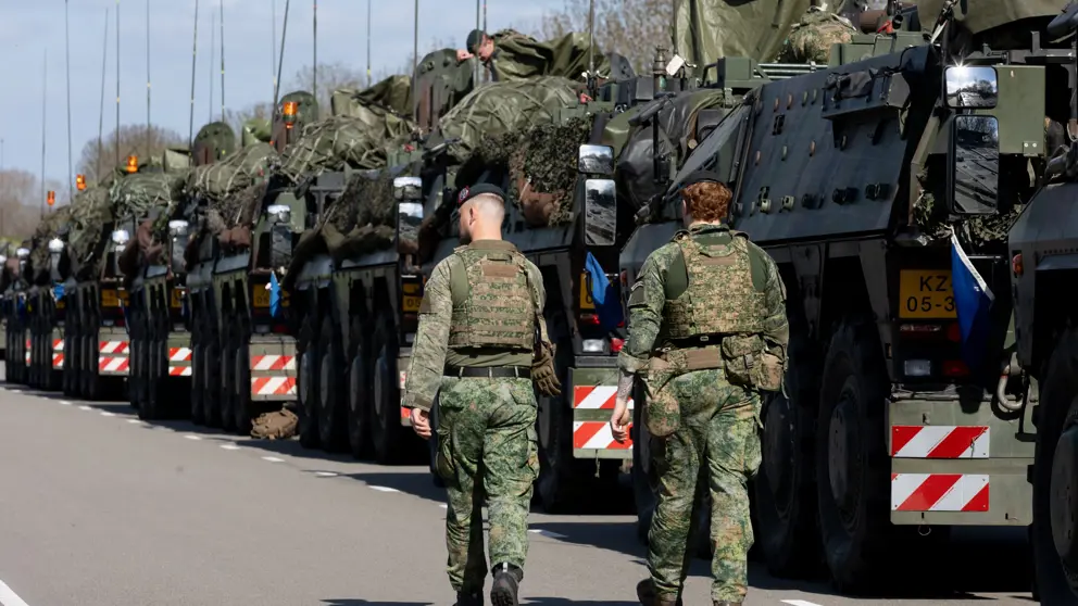 Rij militaire voertuigen. Daarnaast lopen 2 militairen.