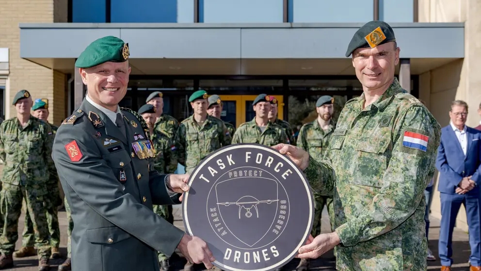 Luitenant-generaal Jan Swillens houdt met collega rond bord vast met de tekst: Task Force Drones. Opgestelde militairen op de achtergrond.