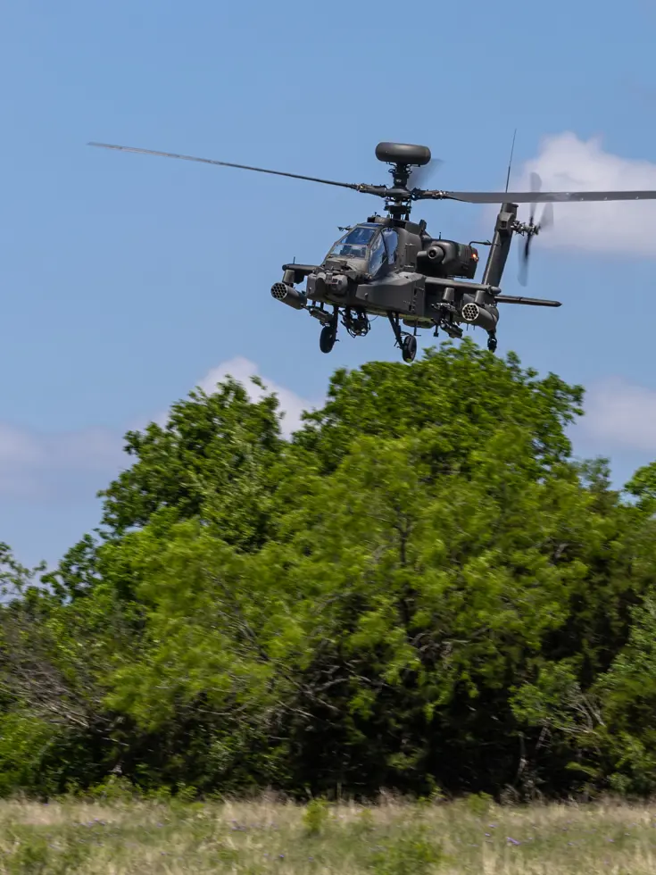 Een laagvliegende Apache boven hoge struiken en gras.