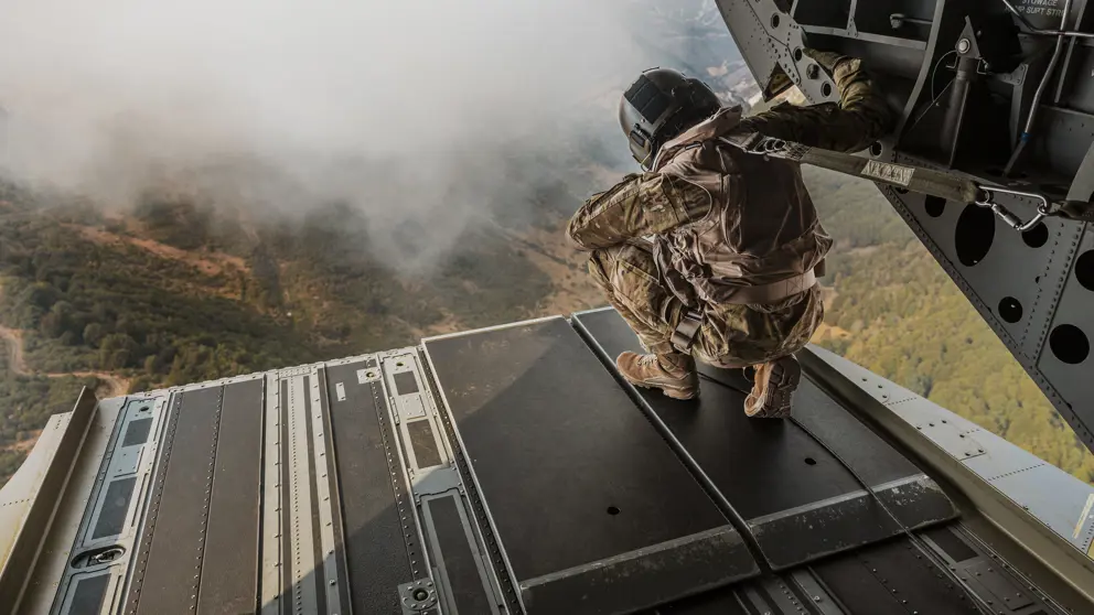 Een militair kijkt vanuit de laadruimte van een helikopter naar beneden.