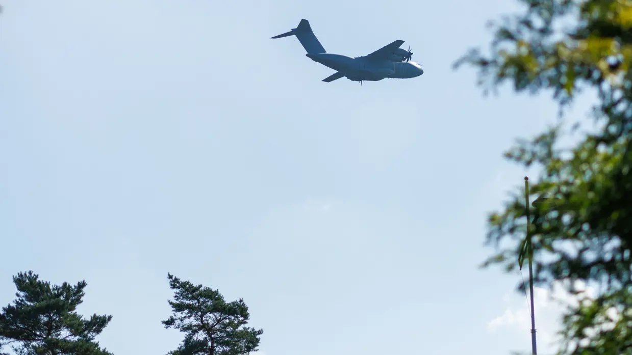 Een A400M vliegt voorbij. Recht en linksonder staan bomen.