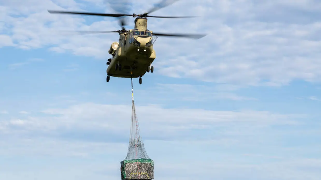 Een Chinook met in de lucht met Bambi Bucket die eronder hangt.