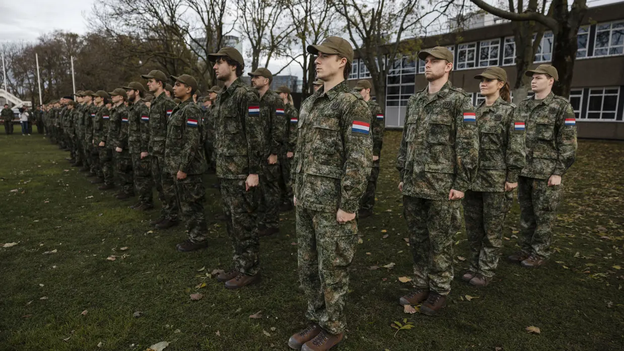 Militairen staan opgesteld. Ze dragen een groen pak en een veldpet.
